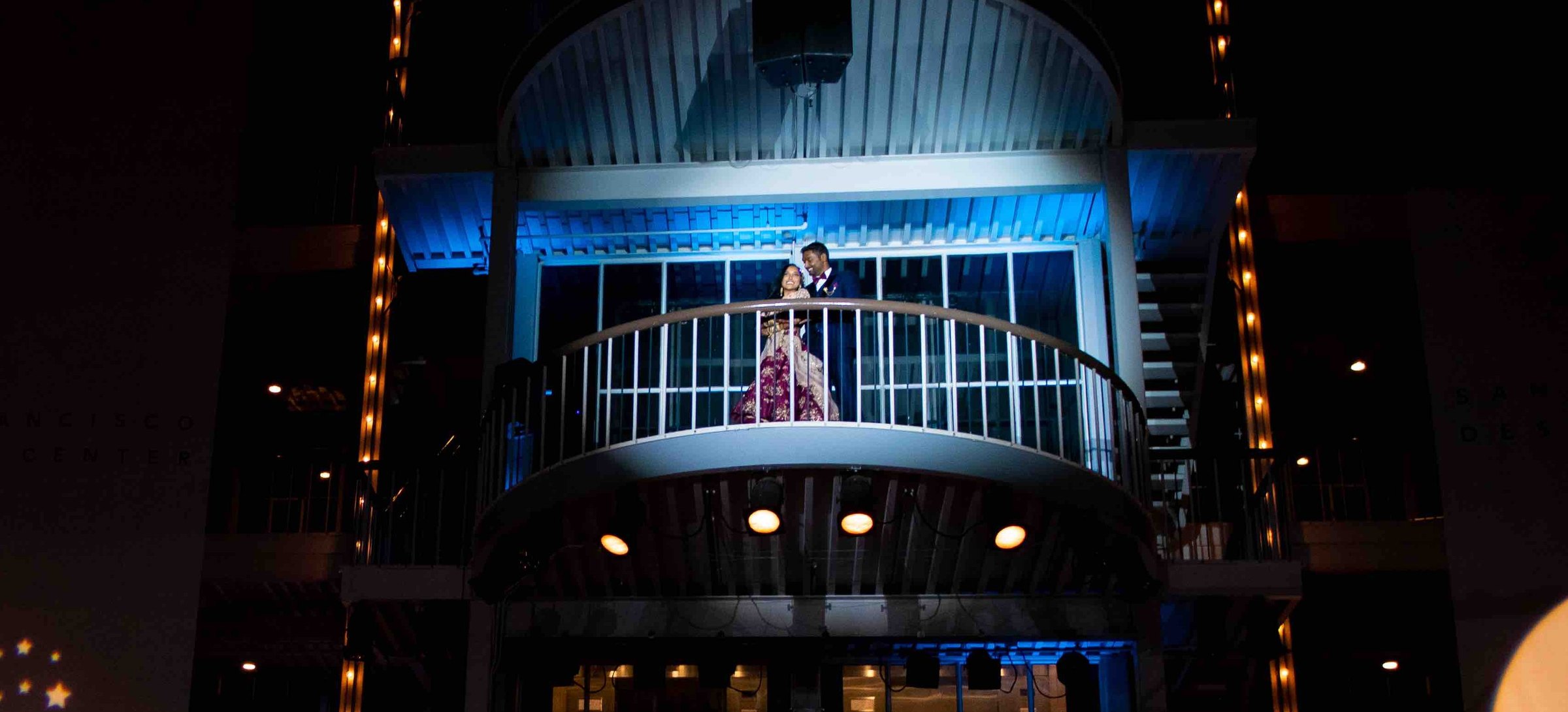 Bride and groom lit by a soft wash light on the balcony above the stage during their reception entrance at the San Francisco Design Center