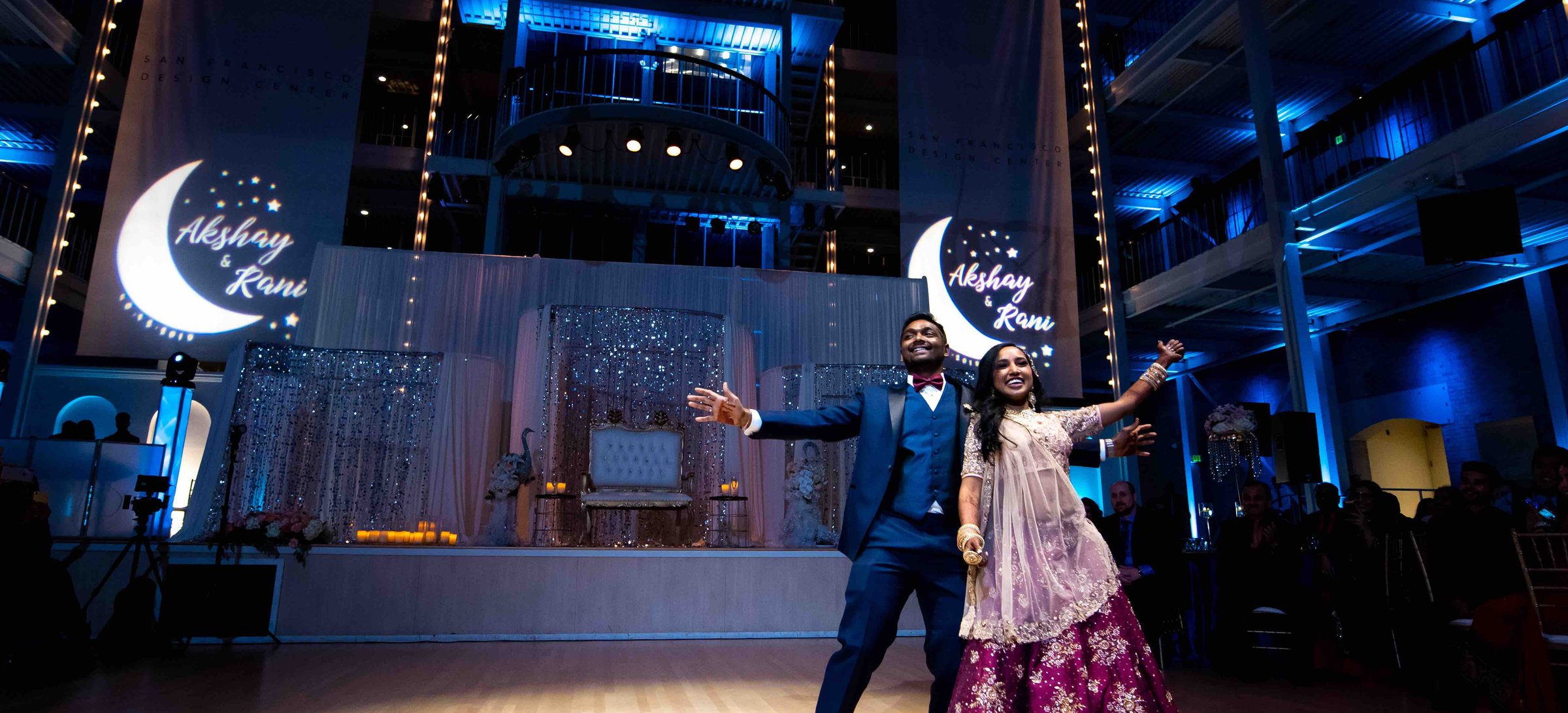 Custom crescent moon monogram with the couple's names projected on two banners above the stage while the couple dances at their reception in the San Francisco Design Center