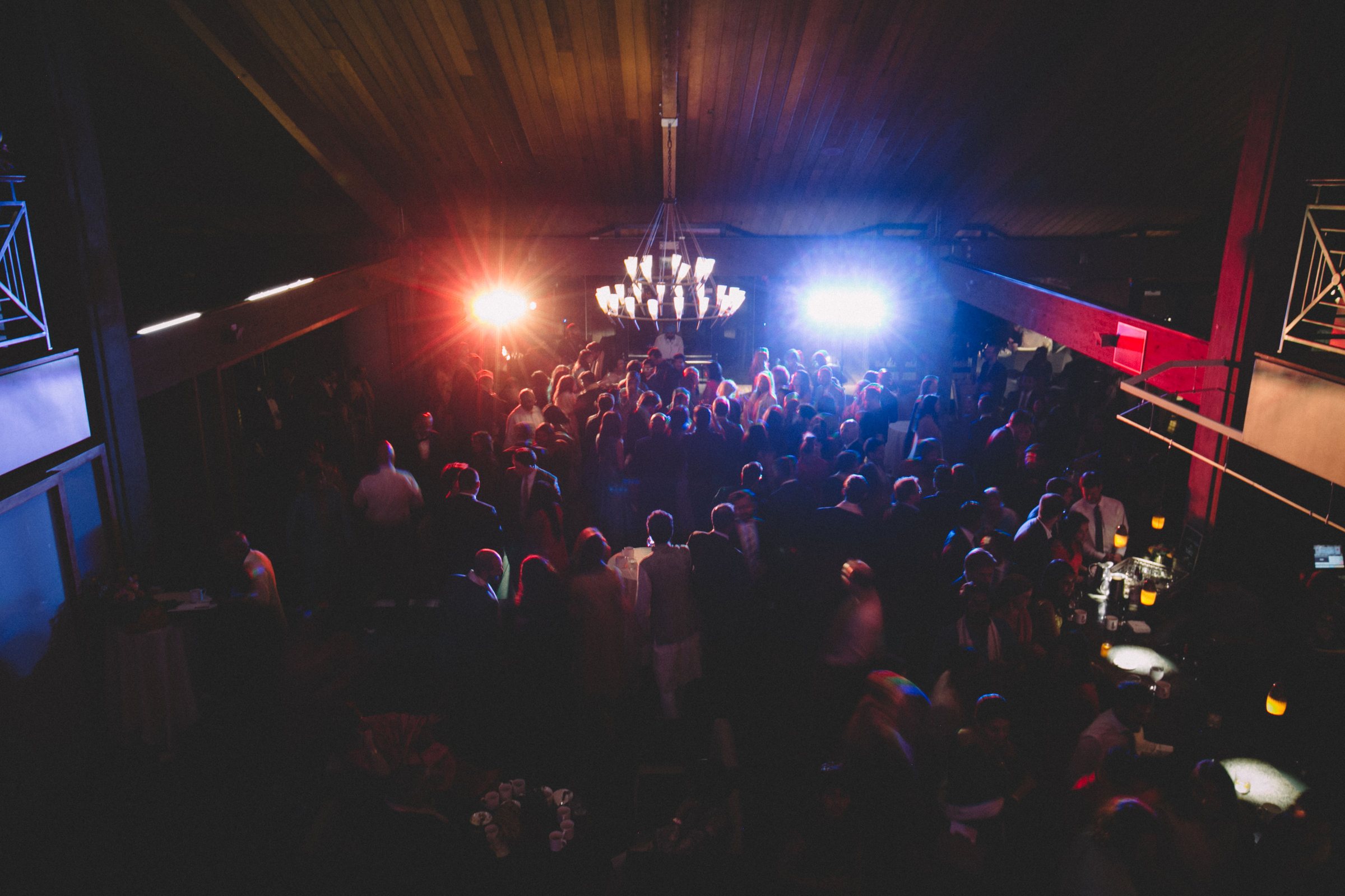 Packed wedding dance floor seen from the balcony, with red and blue intelligent lights behind the DJ booth