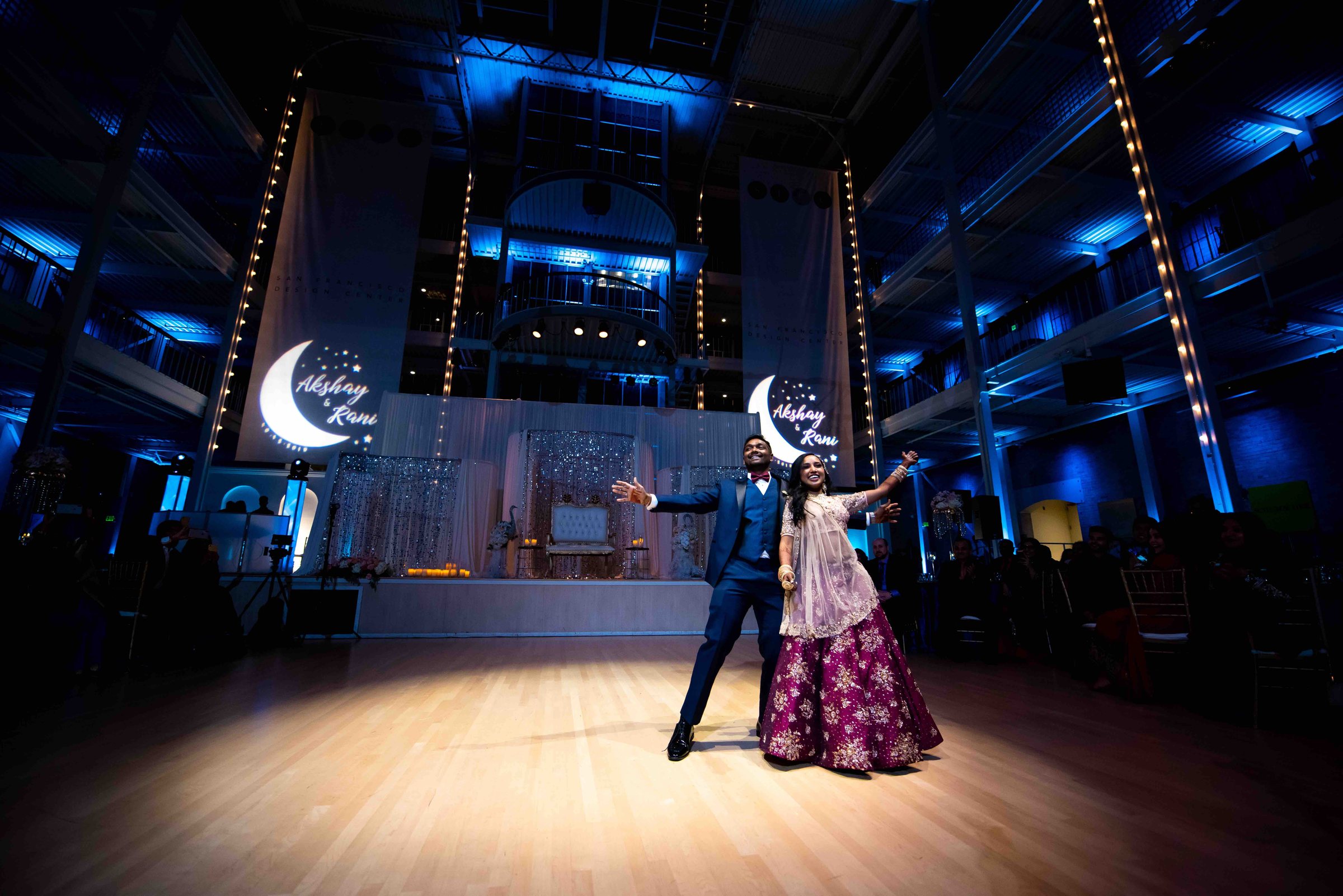 Couple dancing at their reception in the San Francisco Design Center, with the multi level atrium washed in blue uplighting and a custom monogram projected on the banners